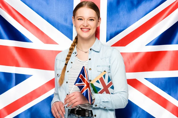 Lächelndes hübsches Mädchen mit Zopf, das Buch auf dem Hintergrund der britischen Flagge hält — Stockfoto