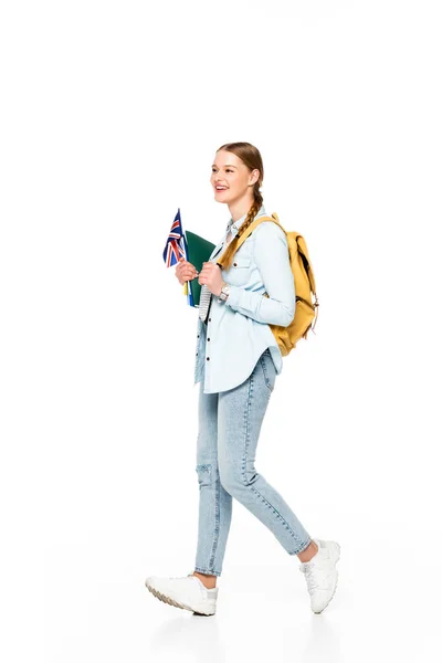 Fille souriante avec tresse et sac à dos marchant avec drapeau du royaume uni et copybooks isolés sur blanc — Photo de stock