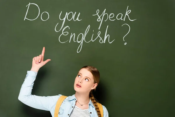 Girl with backpack pointing at chalkboard with do you speak English lettering — Stock Photo