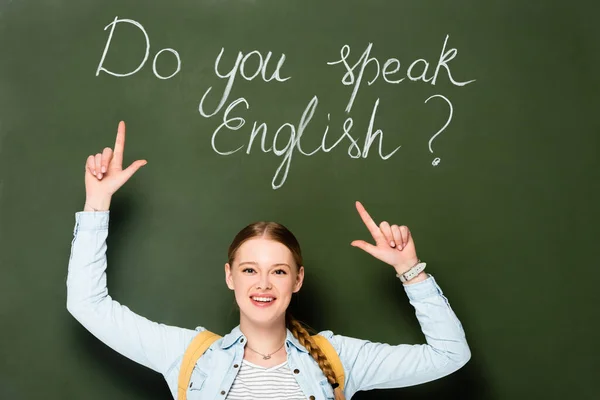 Ragazza sorridente con lo zaino che punta alla lavagna con parli inglese lettering — Foto stock