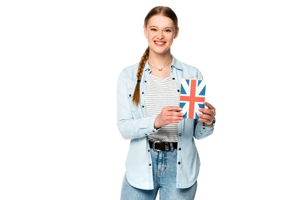 Sorridente bella ragazza con treccia tenendo libro con bandiera del Regno Unito isolato su bianco — Foto stock