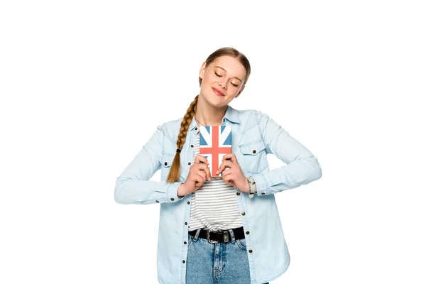 Sorrindo menina bonita com trança e olhos fechados segurando livro com bandeira uk isolado no branco — Fotografia de Stock