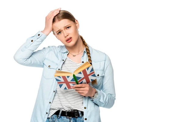 Tensa chica bonita con trenza libro de lectura con bandera del Reino Unido y tocando la cabeza aislada en blanco - foto de stock