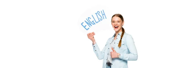Smiling girl with braid holding speech bubble with English lettering and showing thumb up isolated on white, panoramic shot — Stock Photo