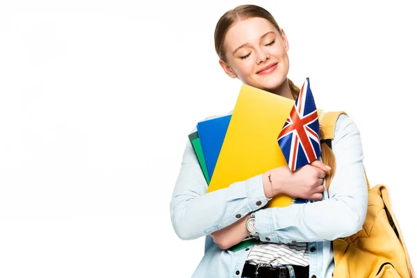 Fille souriante avec sac à dos et les yeux fermés tenant copybooks et drapeau britannique isolé sur blanc — Photo de stock