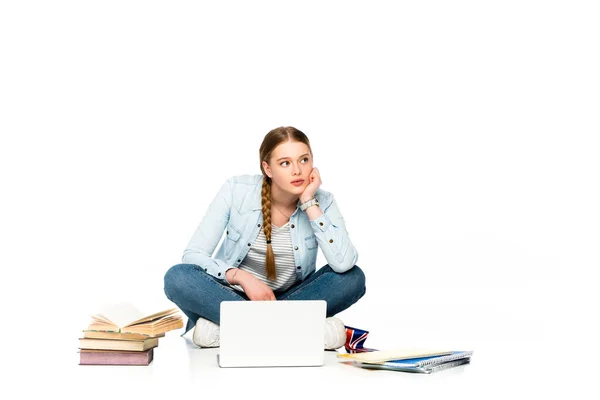 Chica pensativa sentada en el suelo con el ordenador portátil, libros y copybooks y sosteniendo la bandera del Reino Unido aislado en blanco - foto de stock