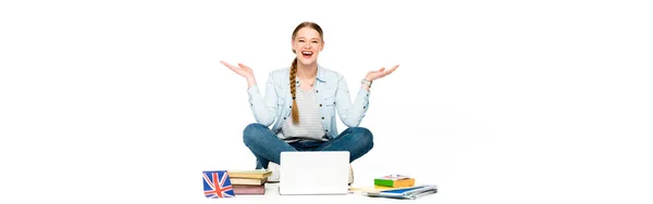 Chica feliz sentado en el suelo con el ordenador portátil, libros y copybooks, bandera del Reino Unido y gesto aislado en blanco, plano panorámico - foto de stock