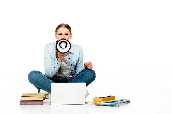 Girl sitting on floor shouting in loudspeaker near laptop, books and copybooks isolated on white — Stock Photo