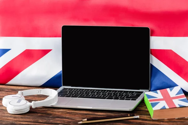 Portátil cerca de libro con bandera del Reino Unido y auriculares en la mesa de madera - foto de stock