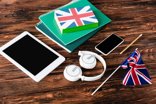 Gadgets near books and copybooks and uk flags on wooden table — Stock Photo