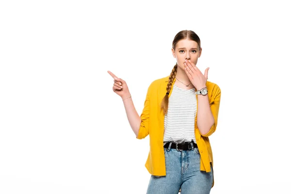 Attractive girl with braid covering mouth with hand and pointing with finger aside isolated on white — Stock Photo