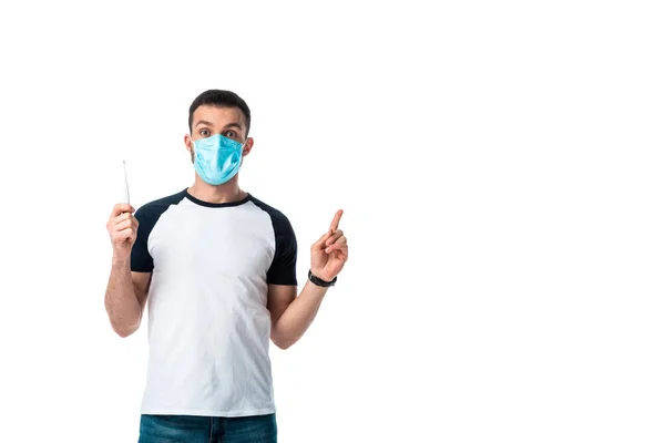 Sick man in medical mask holding digital thermometer and pointing with finger isolated on white — Stock Photo