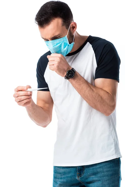 Uomo in maschera medica guardando il termometro digitale e tossendo isolato su bianco — Foto stock