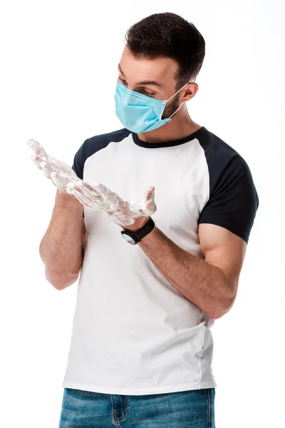 Homme en masque médical et protecteur regardant les mains savonneuses isolées sur blanc — Photo de stock