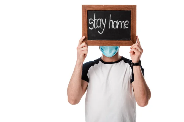 Uomo in maschera medica che copre il viso mentre tiene bordo gesso con soggiorno casa lettering isolato su bianco — Foto stock