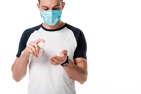 Hombre en máscara médica que sostiene la botella del aerosol con el líquido antibacteriano cerca de la mano aislado en blanco - foto de stock