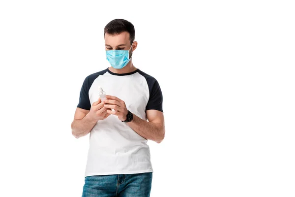 Hombre en máscara médica mirando botella de aerosol con líquido antibacteriano aislado en blanco - foto de stock