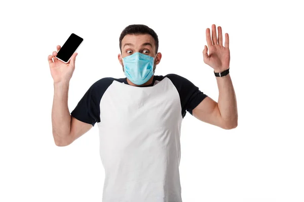Homem chocado em máscara médica segurando smartphone com tela em branco e colocando as mãos para cima isolado no branco — Fotografia de Stock