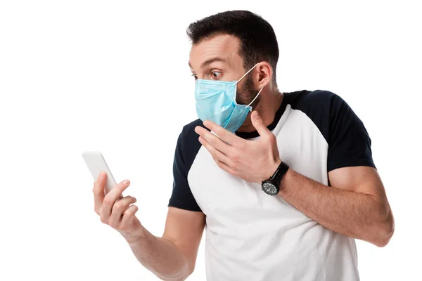 Uomo scioccato in maschera medica guardando smartphone isolato su bianco — Foto stock