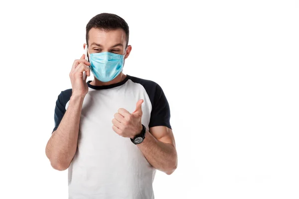 Man in medical mask talking on smartphone and showing thumb up isolated on white — Stock Photo