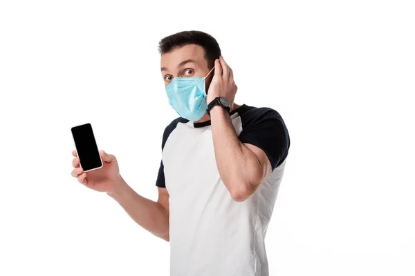 Homme choqué dans le masque médical tenant smartphone avec écran blanc isolé sur blanc — Photo de stock