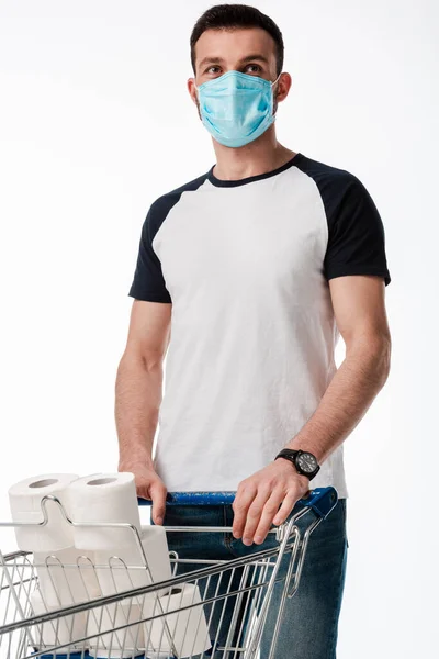 Man in medical mask standing near shopping cart with toilet paper isolated on white — Stock Photo
