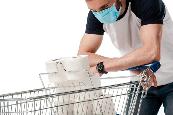 Homem em máscara médica olhando para carrinho de compras com papel higiênico isolado em branco — Fotografia de Stock