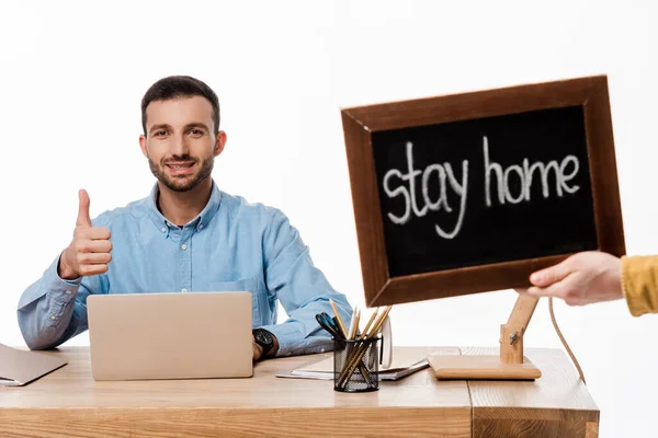 Felice freelance mostrando pollice verso l'alto vicino laptop e lavagna con soggiorno casa lettering isolato su bianco — Foto stock