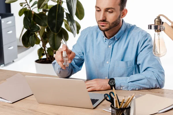Handsome man holding hand sanitizer near laptop isolated on white — Stock Photo