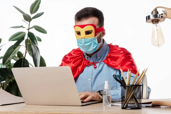 Man in medical mask and superhero costume using laptop isolated on white — Stock Photo