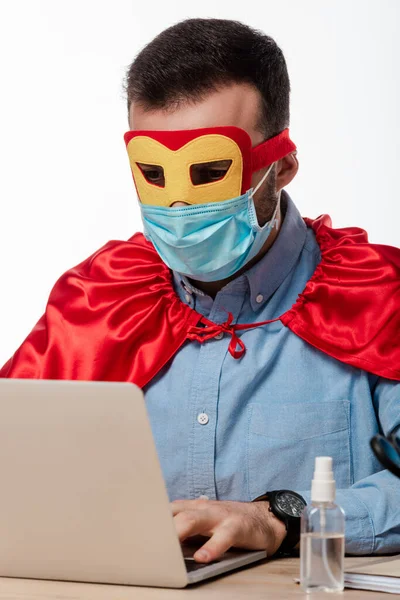 Man in medical mask and superhero cape using laptop isolated on white — Stock Photo