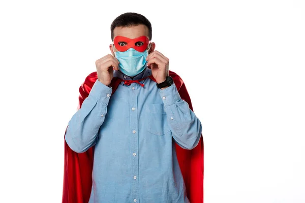 Hombre en traje de superhéroe tocando máscara médica aislado en blanco - foto de stock