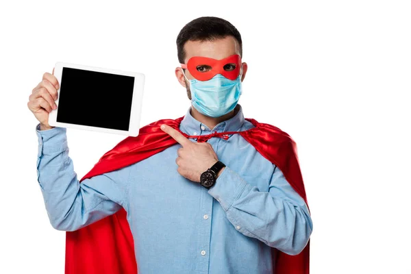 Homme en costume de super-héros et masque médical pointant avec le doigt à la tablette numérique avec écran blanc isolé sur blanc — Photo de stock