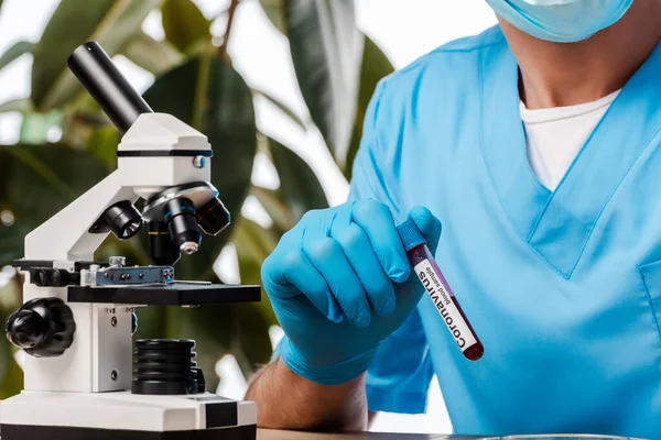 Vista ritagliata dello scienziato in lattice guanto tenuta provetta con campione e coronavirus lettering vicino al microscopio — Foto stock