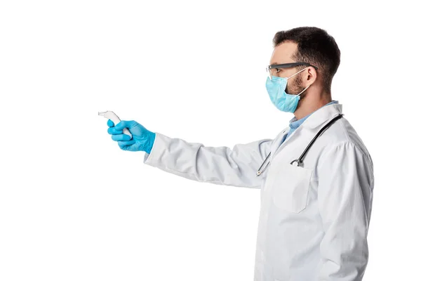 Side view of doctor in medical mask and white coat holding pyrometer isolated on white — Stock Photo