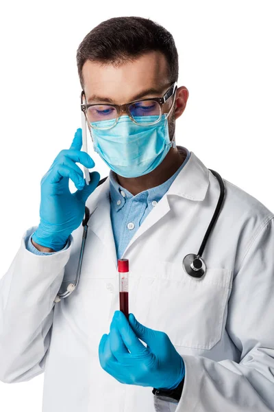 Doctor in medical mask and glasses talking on smartphone while holding test tube with blood sample isolated on white — Stock Photo