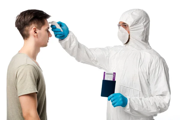 Doctor in personal protective equipment holding pyrometer and passport with boarding pass near man isolated on white — Stock Photo