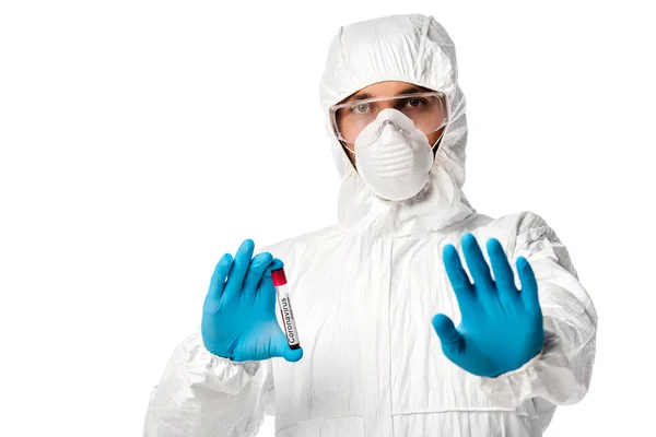 Человек в защитном костюме держит пробирку с образцом крови коронавируса и показывает знак остановки, изолированный на белом — стоковое фото