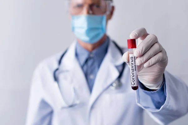 Selective focus of mature doctor in medical mask holding test tube with coronavirus blood sample lettering isolated on grey — Stock Photo