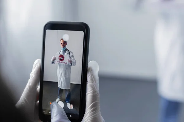 Enfoque selectivo del médico tomando la foto de un hombre maduro con una bata blanca con letras de stop coronavirus a bordo - foto de stock