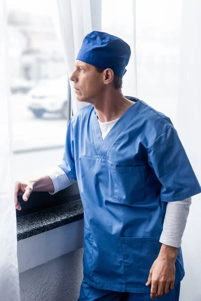 Médecin d'âge moyen en chapeau de gommage bleu regardant la fenêtre — Photo de stock