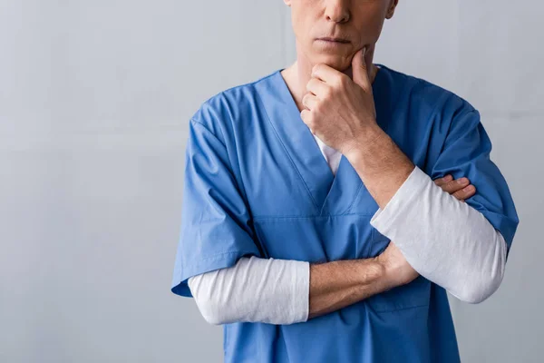 Cropped view of middle aged doctor touching face while thinking on grey — Stock Photo