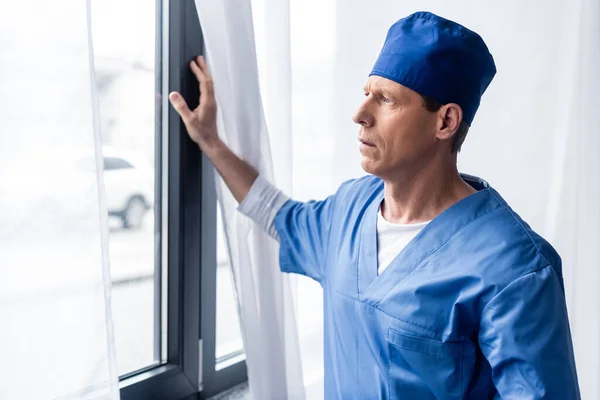 Médico maduro en sombrero de matorral azul mirando a la ventana - foto de stock