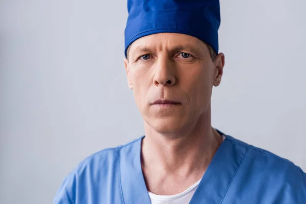Middle aged doctor in blue scrub hat isolated on grey — Stock Photo