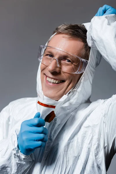Hombre feliz y maduro en traje de hazmat y gafas aisladas en gris - foto de stock