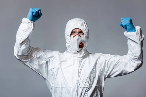 Uomo maturo in tuta hazmat, maschera medica e occhiali in piedi con pugni serrati isolati su grigio — Foto stock