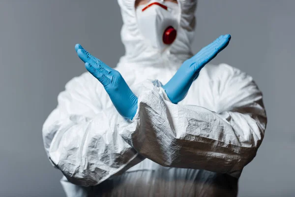Vista recortada del médico maduro en traje de materiales peligrosos, máscara médica y guantes de látex de pie con brazos cruzados aislados en gris - foto de stock