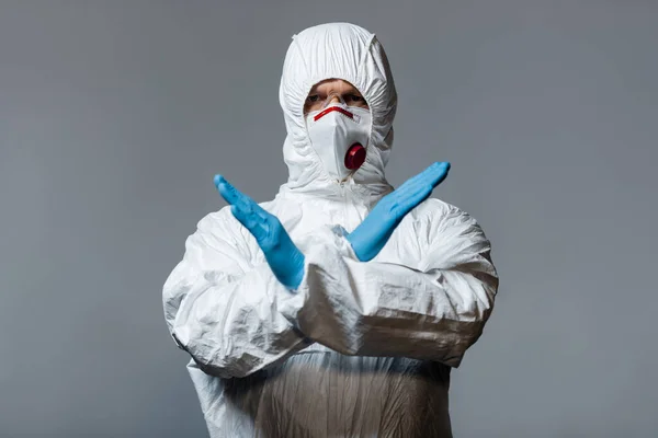 Médico maduro em terno hazmat, máscara médica e luvas de látex de pé com braços cruzados isolados em cinza — Fotografia de Stock
