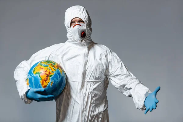 Homme en combinaison Hazmat et masque médical tenant globe et geste isolé sur gris — Photo de stock