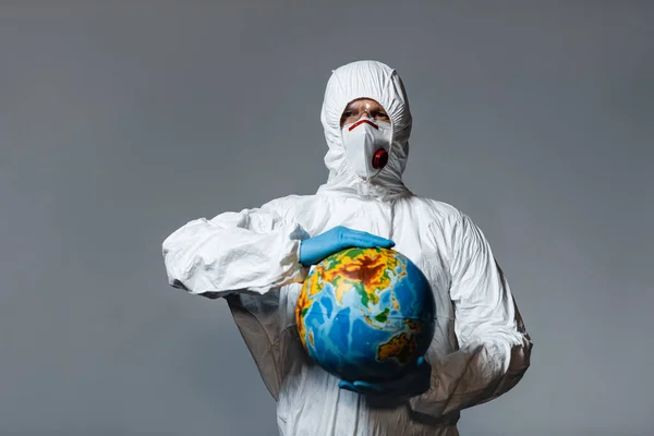 Homem em equipamento de proteção individual segurando globo isolado em cinza — Fotografia de Stock